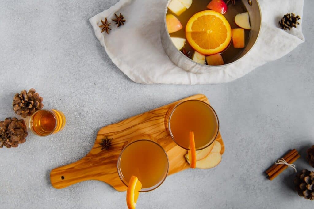 Overhead shot of mulled apple cider in a pot with two glasses filled with spiked apple cider.