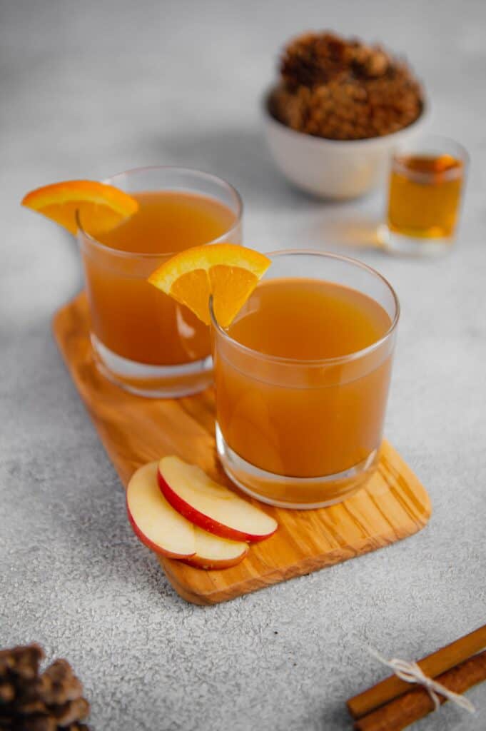 Two glasses garnished with an orange slice of spiked apple cider.