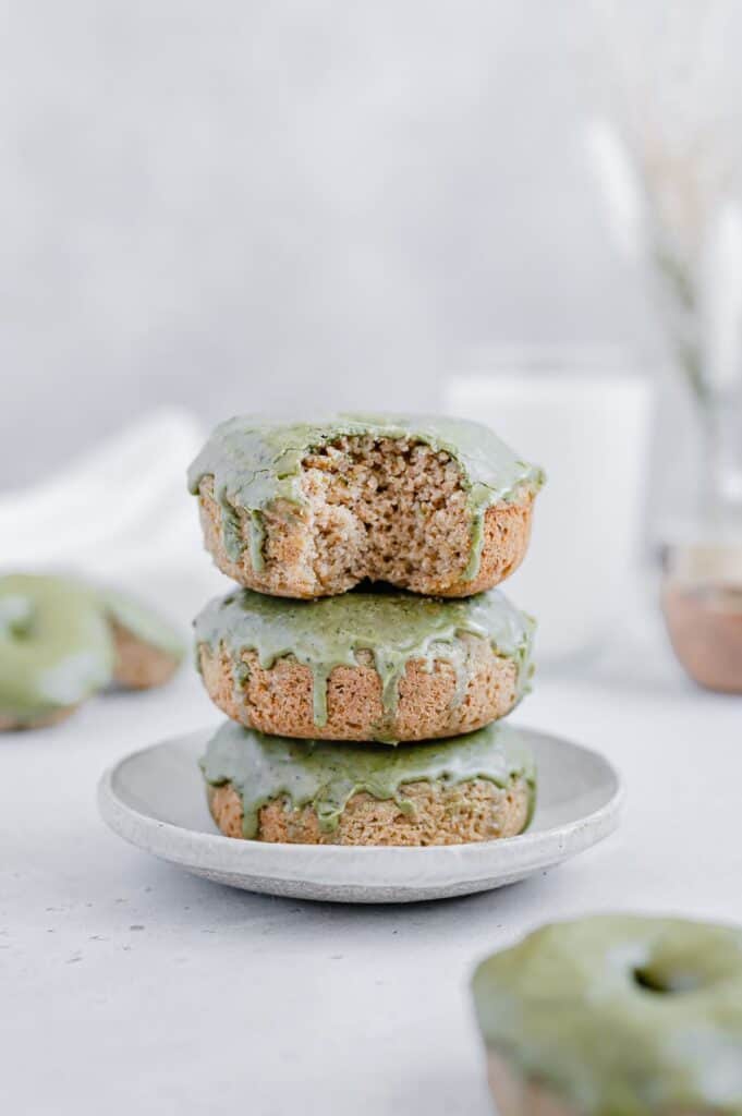 Three matcha glazed donuts stacked on a plate and the top donut has a bite taken out of it.