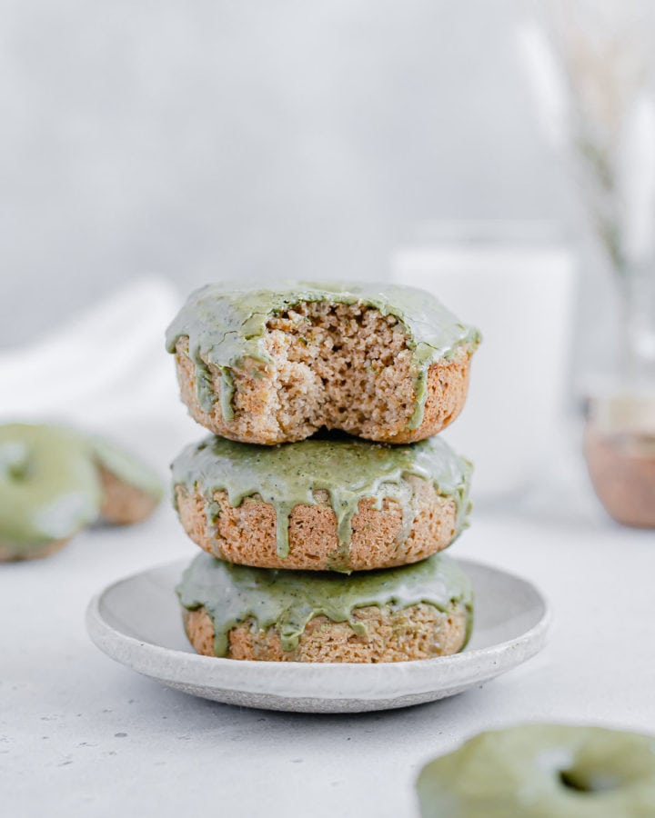 Three matcha glazed donuts stacked on a plate and the top donut has a bite taken out of it.