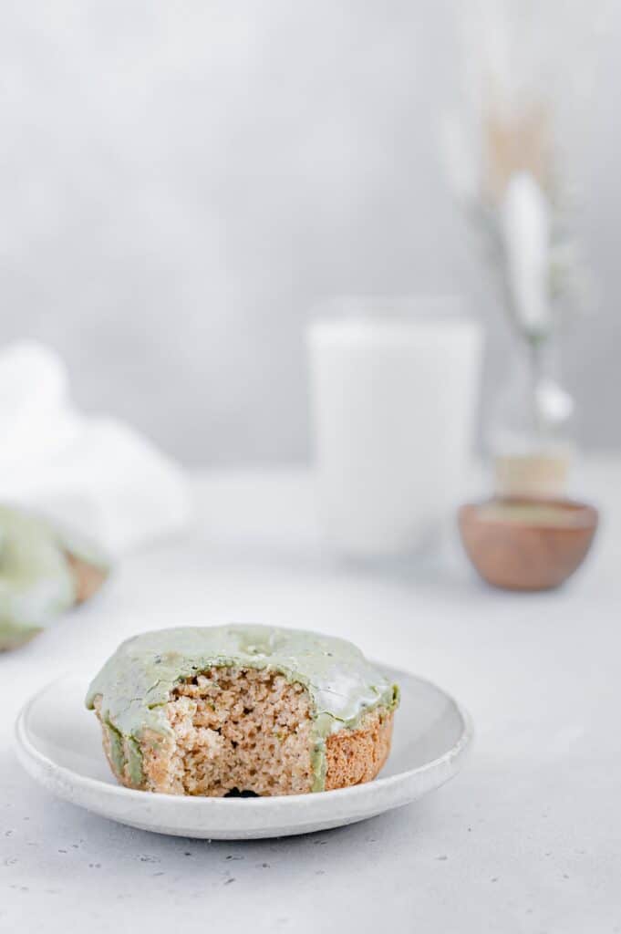 A matcha glazed donut with a bite taken out of it on a plate.