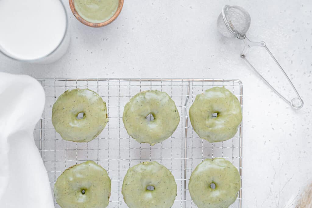 Overhead of matcha donuts on a cooling rack with a dusting wand on the side.