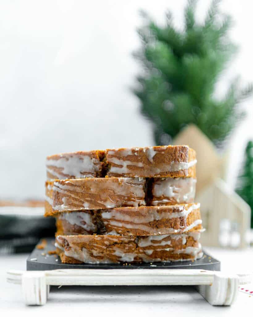 Photo of four gingerbread loaf sliced and stacked on top of one another with a Christmas tree in the background.