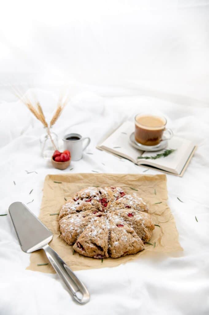 45 degree angle of vegan strawberry rosemary scones with a cup of coffee and strawberries in the background.