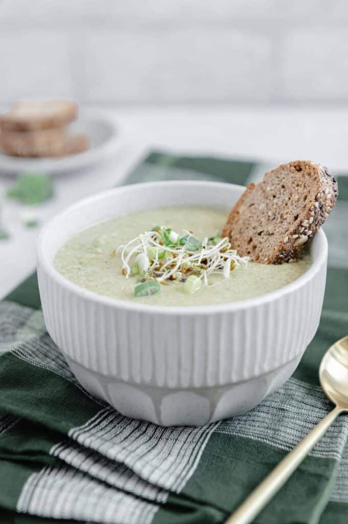 A bowl of broccoli soup with a piece of toasted bread dipped in it.