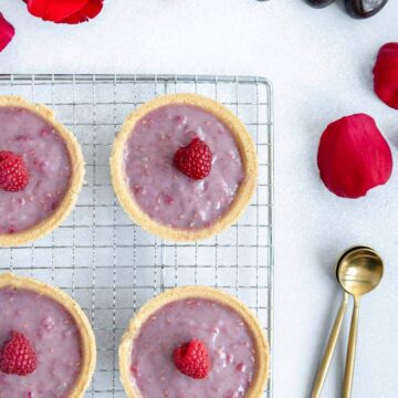 For raspberry tarts on a cooling rack with chocolate and rose petals scattered around.