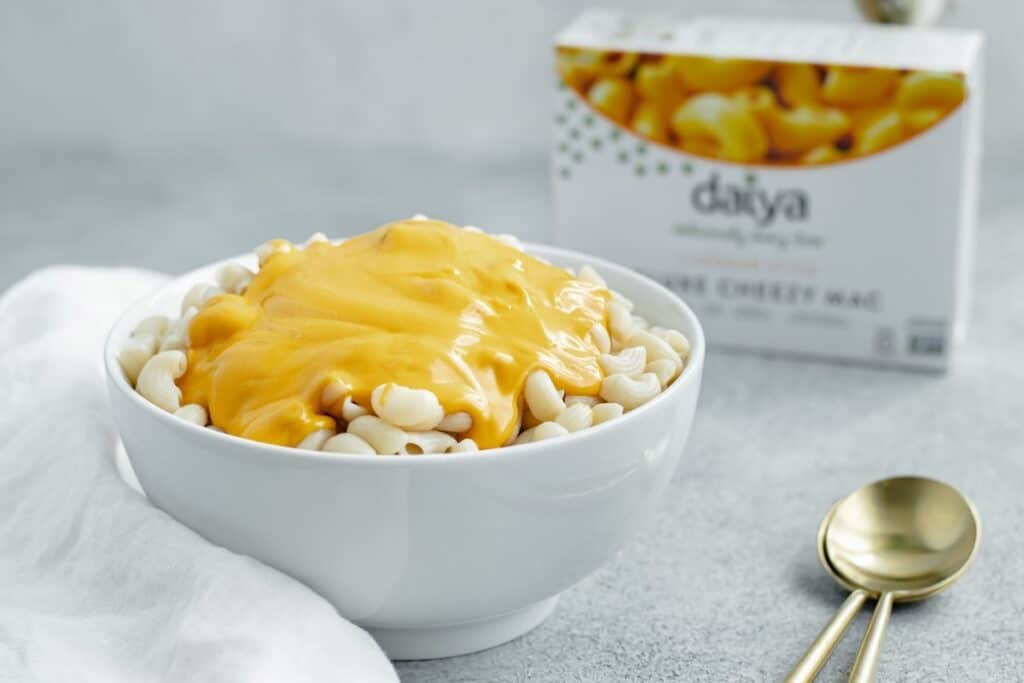 A bowl of macaroni with cheese poured over top and a Daiya mac and cheese box in the background.