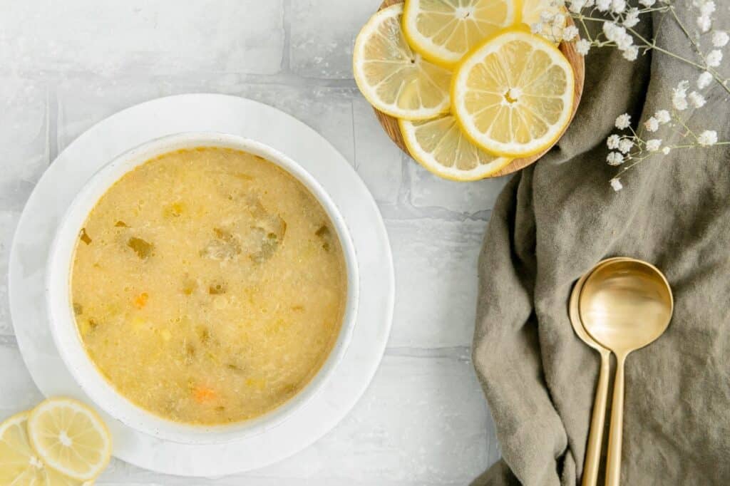Overhead of lemon orzo soup with a linen napkin with spoons on top and lemons on the side.