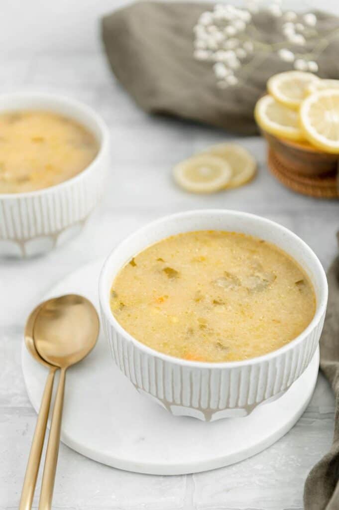 Lemon soup on top of a marble tray with spoons on the side and lemons in the background.