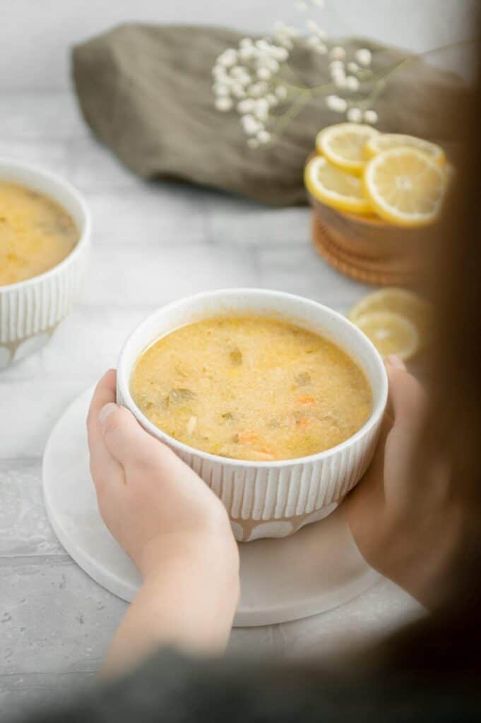 Hands grabbing a bowl of vegan lemon orzo soup/