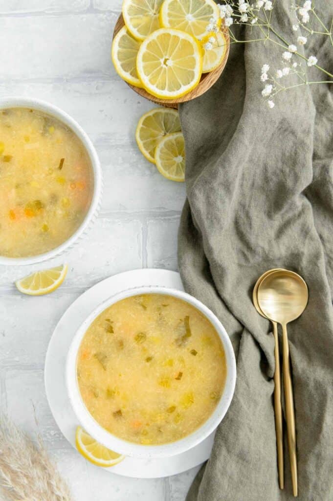 Overhead of two bowls of lemon soup with two spoons, a linen napkin and lemons off to the side.