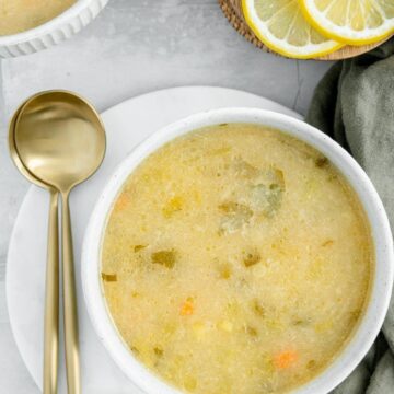 Overhead of a vegan lemon orzo soup with lemons scattered around and two spoons on the side.