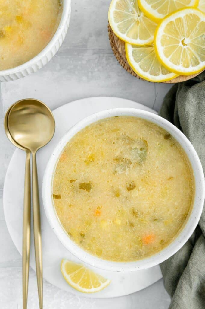 Overhead of a vegan lemon orzo soup with lemons scattered around and two spoons on the side.