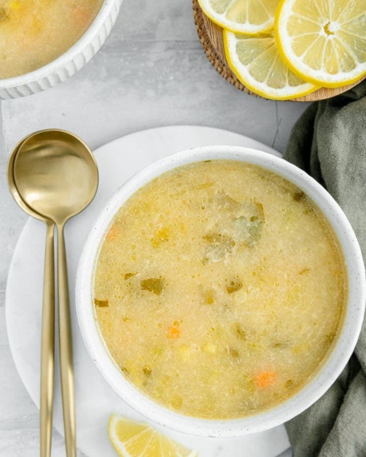 Overhead of a vegan lemon orzo soup with lemons scattered around and two spoons on the side.