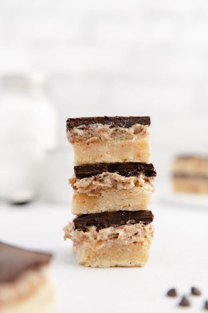 Three squares of vegan millionaire shortbread cookies stack on top of one another.