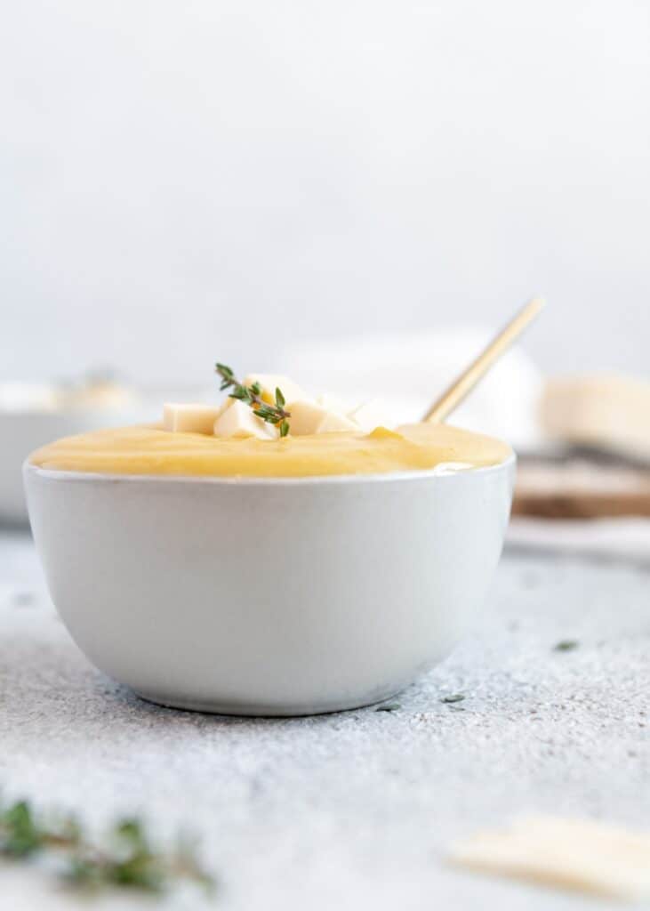 Bowl of pumpkin soup with cubed cheese and thyme as a garnish.