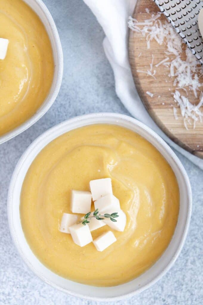 Overhead of a pumpkin soup bowl with cubed cheese on top.