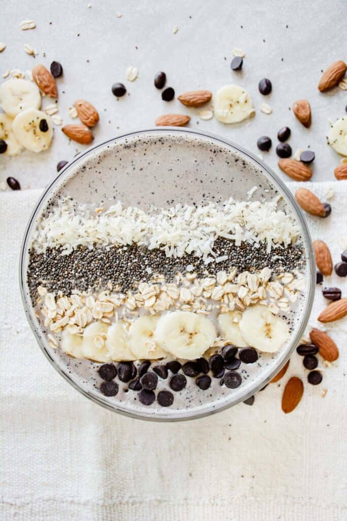Overhead of a coffee banana smoothie bowl topped with chocolate chips, banana, oats, chia seeds and coconut.