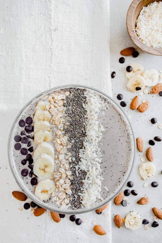Overhead of a coffee banana smoothie bowl topped with chocolate chips, banana, oats, chia seeds and coconut.