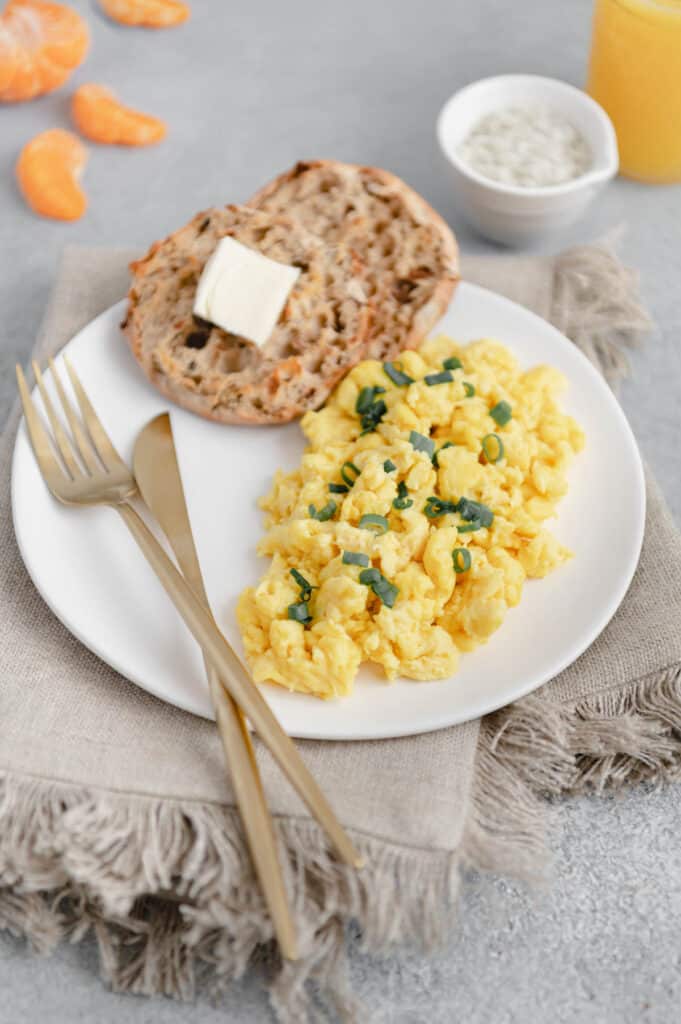 Just eggs on a plate with English muffins and oranges and orange juice in the background.