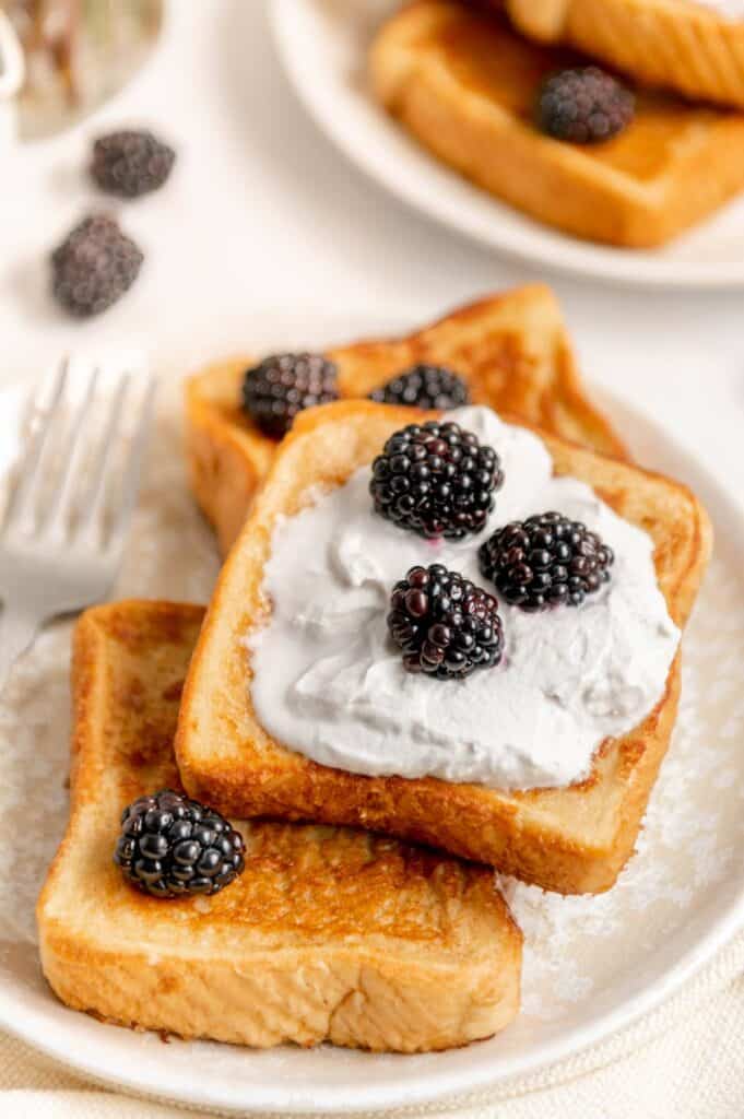 Up close of a stack of vegan French toast, topped with whipped cream and blackberries.