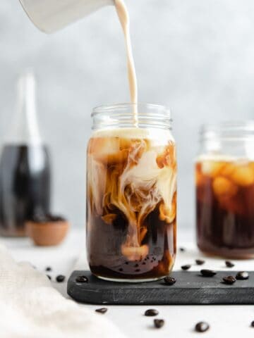 Iced coffee with creamer being poured into it.