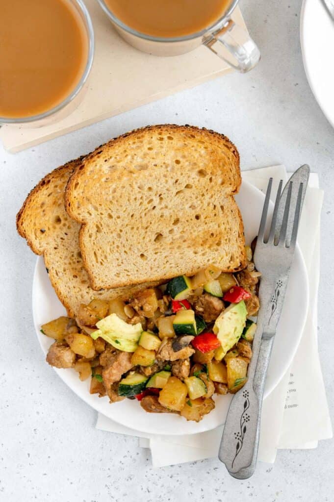 Overhead of savory hash with toast and a fork and knife on the side.