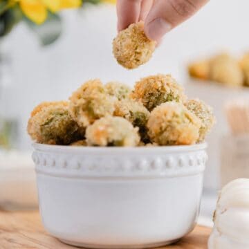 A hand reaching for vegan fried olives, the perfect bite-sized snack that you can pop in your mouth!