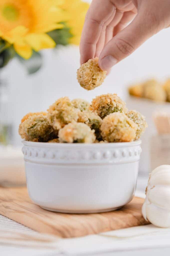 A hand reaching for vegan fried olives, the perfect bite-sized snack that you can pop in your mouth!