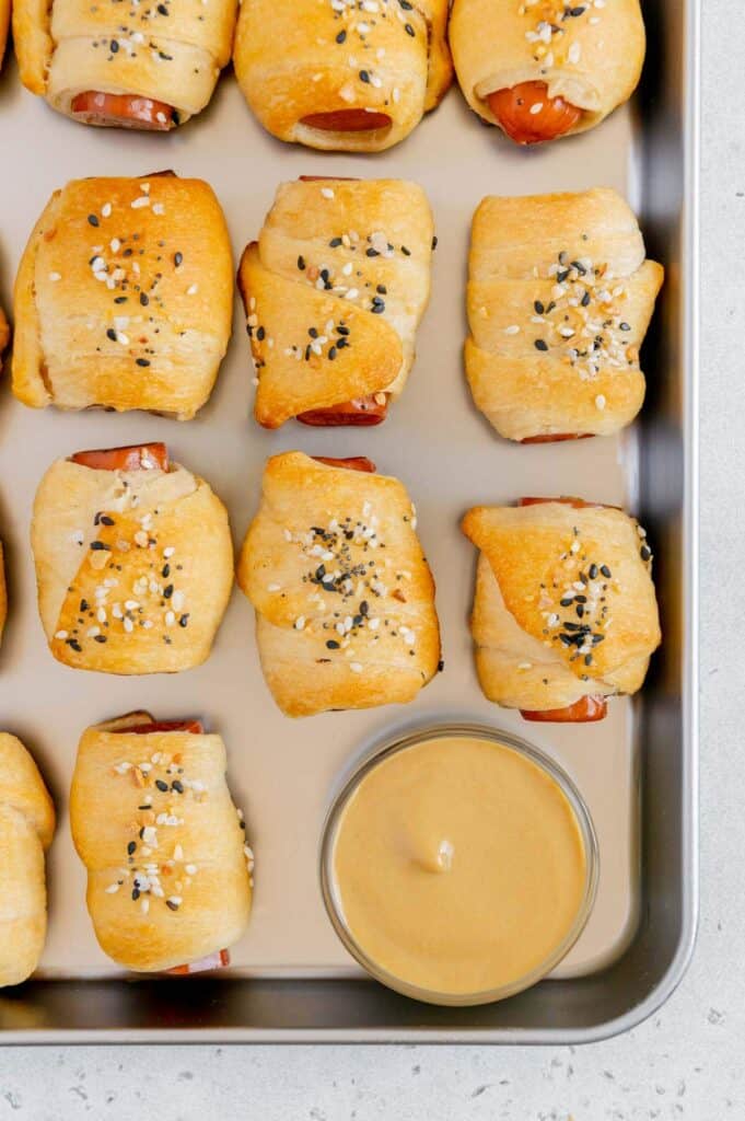 Freshly baked hot dogs wrapped in Pillsbury Crescent Rolls on a baking sheet.