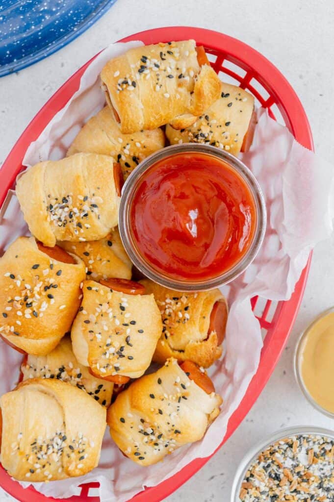 Overhead of golden brown vegan pigs in a blanket with ketchup in a basket.