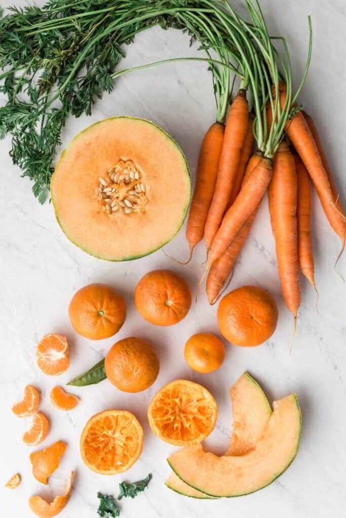 Overhead of orange fruits and vegetables - carrots, melon, and oranges.