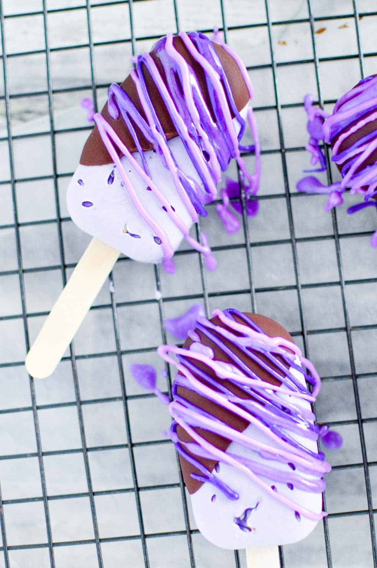 Vegan lavender ice cream bars dipped in chocolate with purple royal icing drizzle.