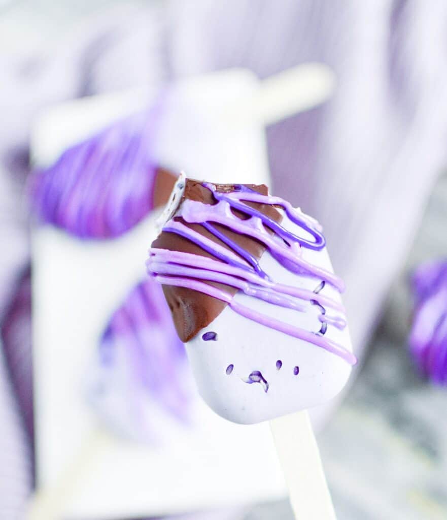 Half eaten lavender chocolate dipped ice cream bar drizzled with purple royal icing.