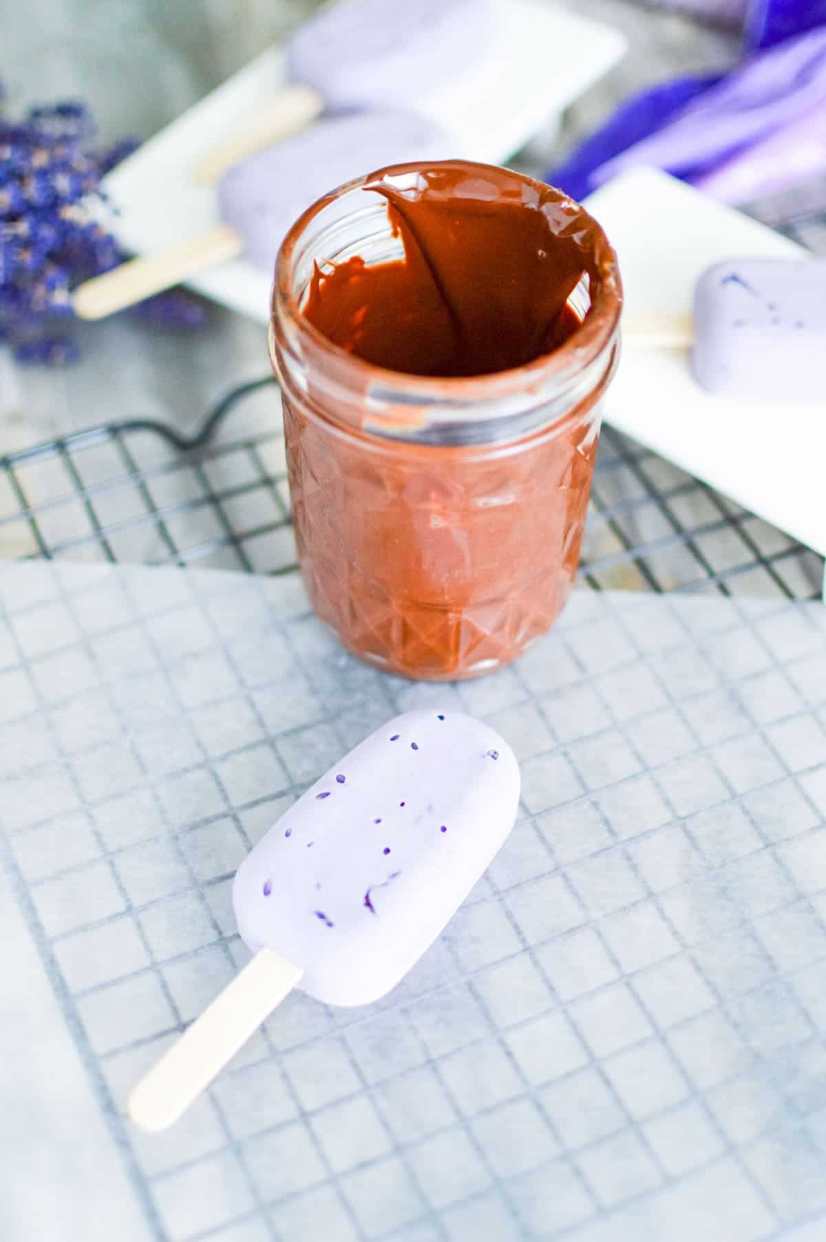 Mini vegan lavender ice cream bar next to melted chocolate in a mason jar waiting to be dipped.