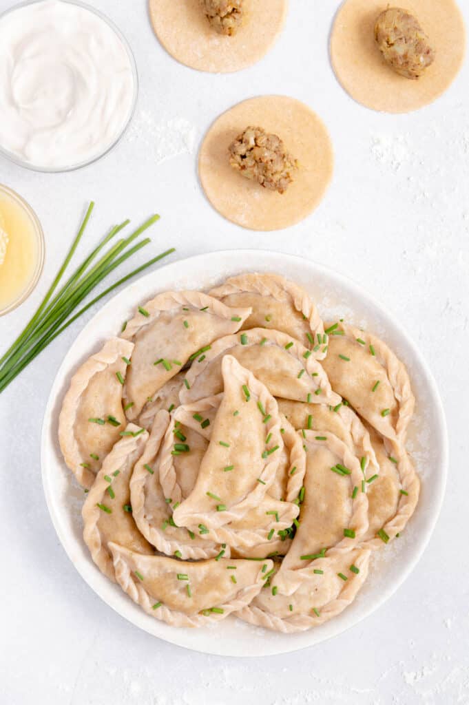 A plate full of vegan pierogies with fresh chives overtop.