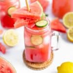 Summer watermelon drink in a mason jar with watermelon, lemon and mint scattered around.