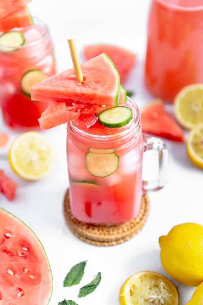 Summer watermelon drink in a mason jar with watermelon, lemon and mint scattered around.