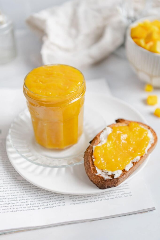 A full jar of homemade jam on a plate with a piece of toast.