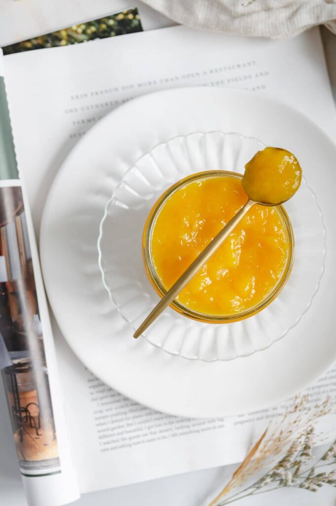 Overhead of a jam jar with a spoon full of jam on top of a magazine.