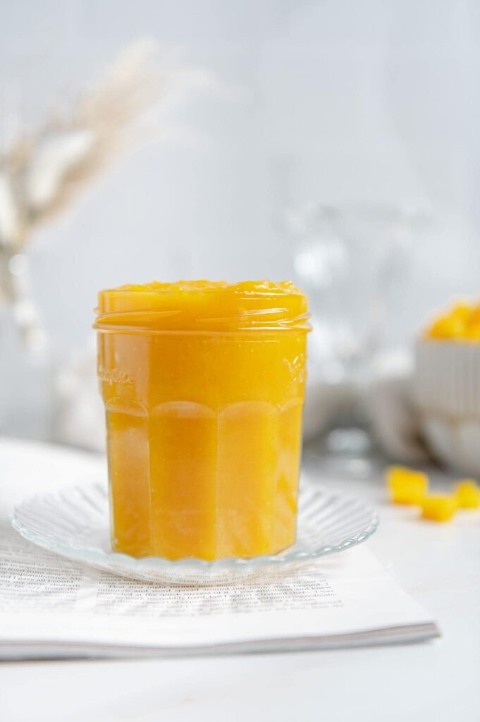 Homemade mango jam in a glass jar on a saucer.