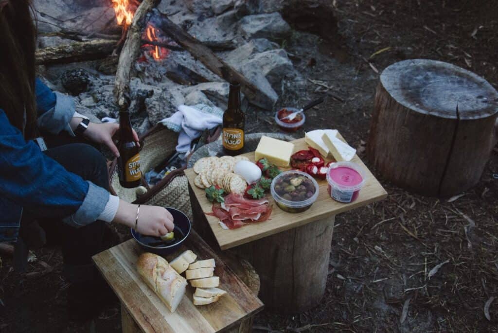 Girl sitting by a campfire enjoying a charcuterie board.