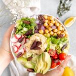 Hands holding up the perfect lunch - a Mediterranean buddha bowl.