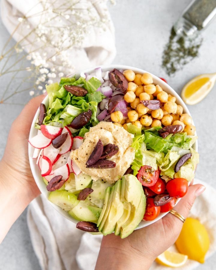 Hands holding up the perfect lunch - a Mediterranean buddha bowl.