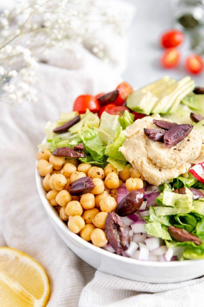 Upclose of a Mediterranean bowl showing garbanzo beans, olives, lettuce, and red onion.