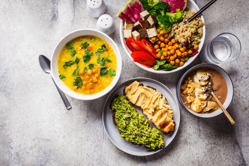 Overhead of different vegan meals - curry, avocado toast, rice bowl, and a smoothie bowl