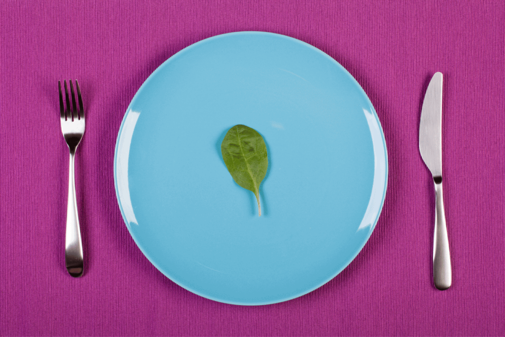 A blue plate with one piece of spinach on it.