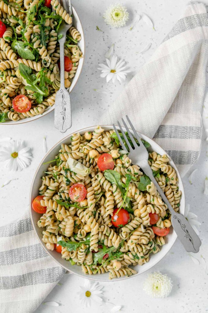 Overhead of two vegan pesto pasta salads in bowls with forks.