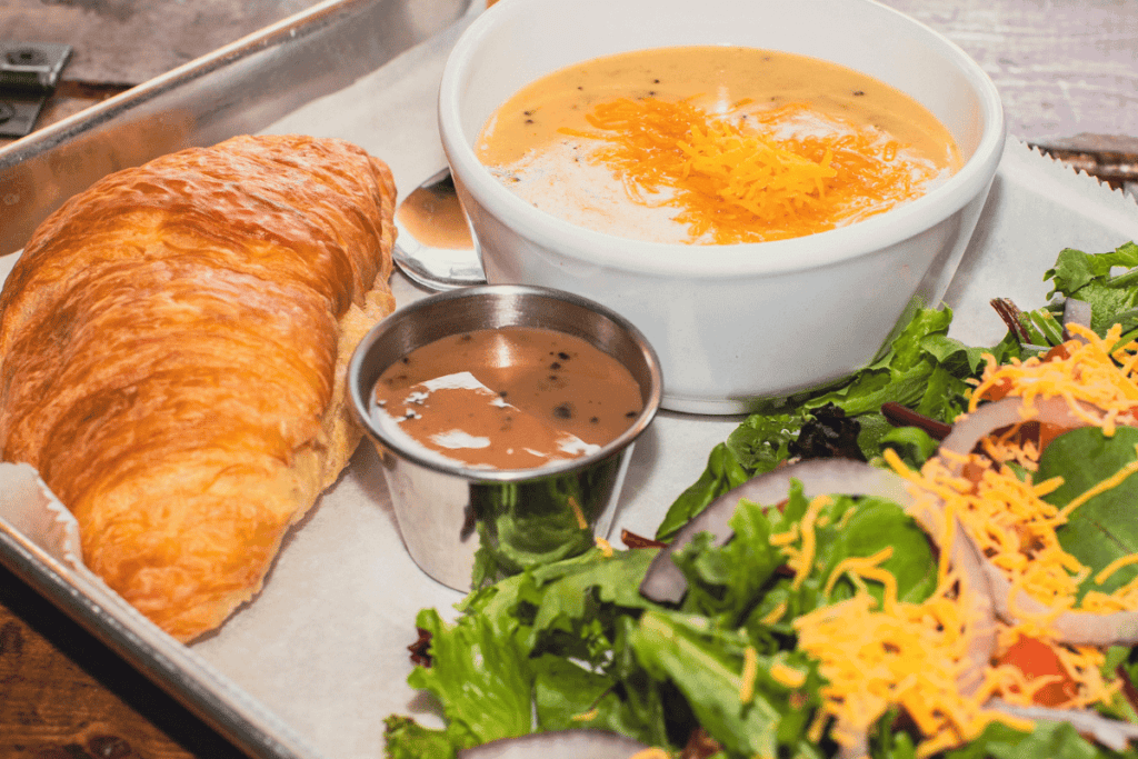 A lunch plate with a soup, salad, and croissant.