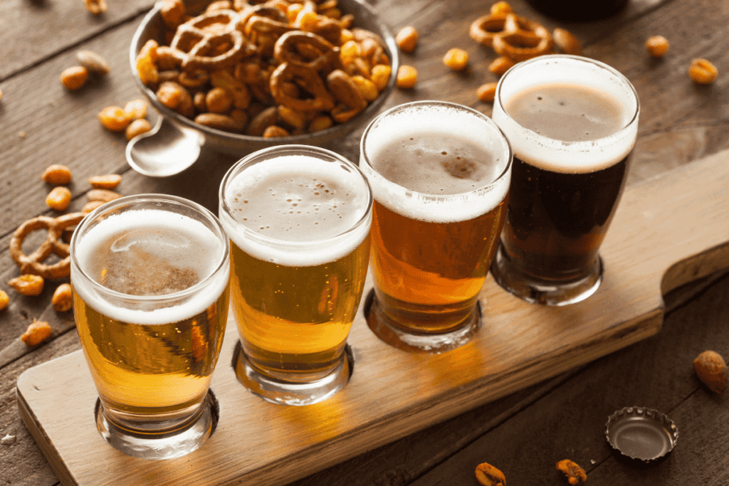 A flight of beer with pretzels and nuts on the side.